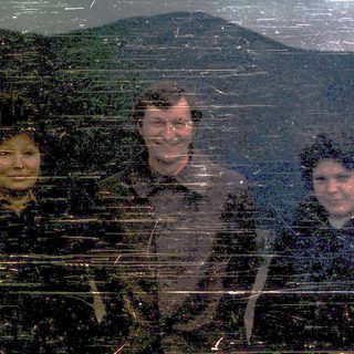 Three people smiling in a bus window during snowfall.