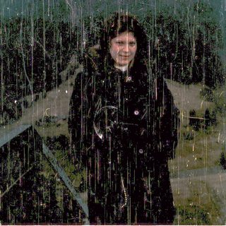 Person smiling in heavy rain outdoors.