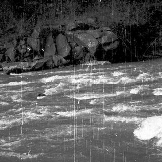 Rain falling on turbulent nighttime river with rocky background.