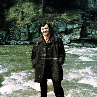 Person standing by a fast-flowing river in a forest.