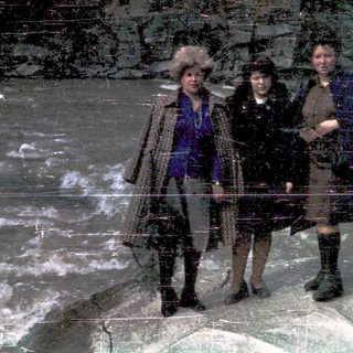 Three women standing on icy terrain near flowing water.