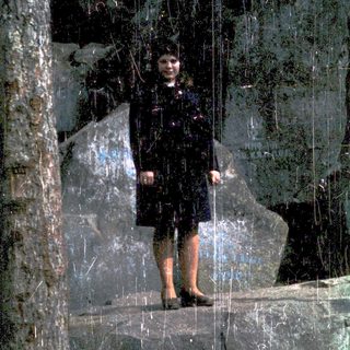 Girl standing in reflective glass with dark background.