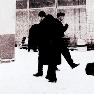 Two men walking with luggage in snowy outdoor area.