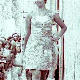 Woman in dress walking down crowded outdoor runway.