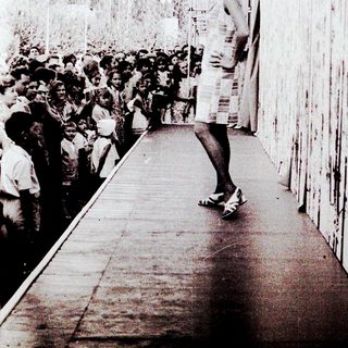 Person standing alone on a platform near a crowd.