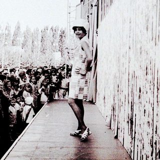 Person standing alone on a platform near a crowd.
