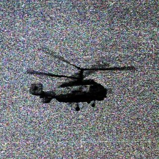 Helicopter flying over open, grassy field.