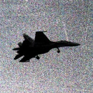Jet aircraft in mid-flight over open landscape.