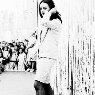 Woman in 1960s dress speaking into phone on city street.