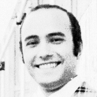 Smiling man in plaid blazer posing outdoors.