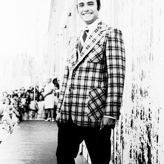 Smiling man in plaid blazer posing outdoors.