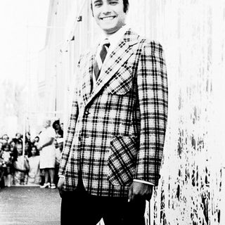 Smiling man in plaid blazer posing outdoors.