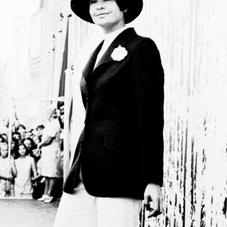 Elegant woman in 1940s attire posing outdoors.