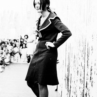 Young woman in 1960s-style dress walking confidently.
