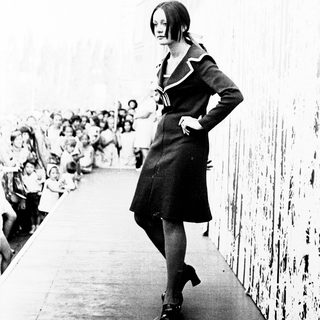 Young woman in 1960s-style dress walking confidently.