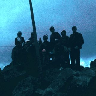 Group of people standing on rocky shore at dusk.