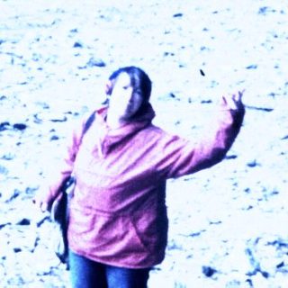 Person standing on rocky mountain ridge near wooden cabin.