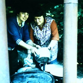 Two women preparing food outdoors over large pot.