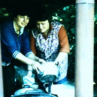 Two women preparing food outdoors over large pot.