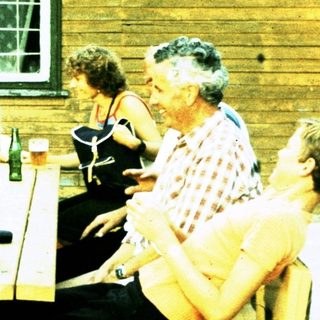 Group socializing outdoors at rustic wooden building.
