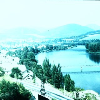 Scenic river valley with bridge, houses, and hills.