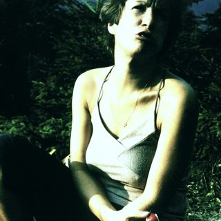 Person sitting outdoors in natural setting, holding cigarette.
