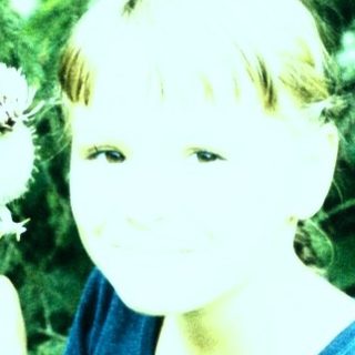 A child holding dandelions in a green outdoor setting.
