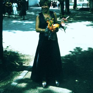 Person in black dress holding flowers outdoors.