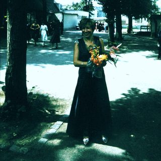 Person in black dress holding flowers outdoors.