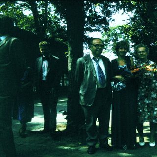Group of people posing outdoors with floral wreath.