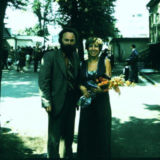 Two people holding floral offerings outdoors near trees.