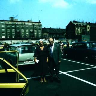 Two people standing in a mid-20th-century parking lot.