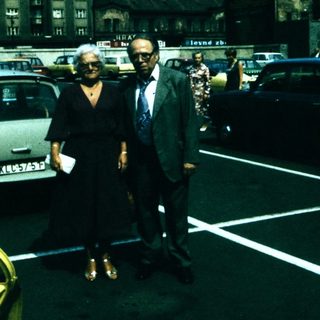 Two people standing in a mid-20th-century parking lot.