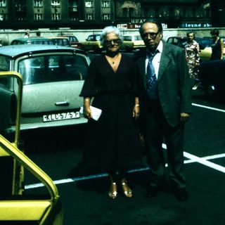 Two people standing in a mid-20th-century parking lot.