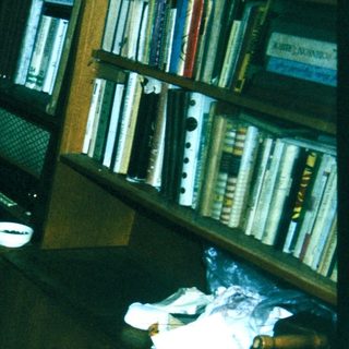 Person sleeping on office floor surrounded by books and papers.