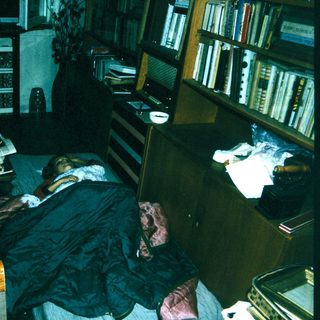 Person sleeping on office floor surrounded by books and papers.