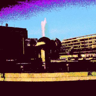 Urban fountain with modern buildings at dusk.
