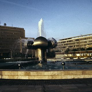 Modernist fountain in urban plaza with tall buildings.
