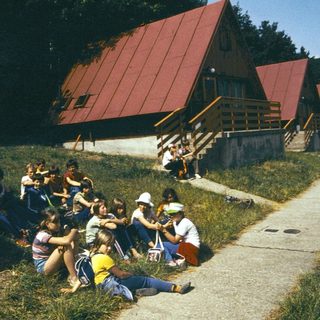 Group of people gathered outdoors near lakeside cabin.