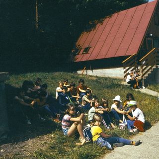 Group of people gathered outdoors near lakeside cabin.