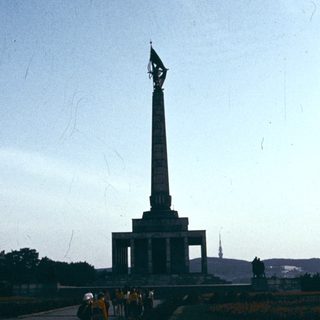 Tall Soviet-era monument with flag, people walking nearby.