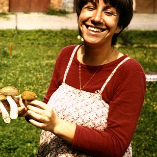 Woman smiling while holding wild mushrooms outdoors.