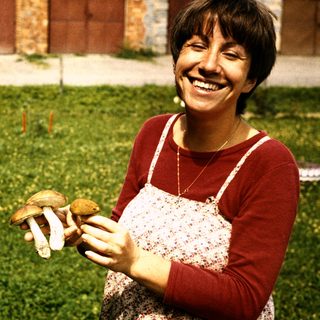 Woman smiling while holding wild mushrooms outdoors.