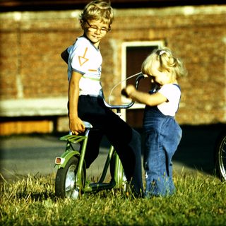 Three children playing with bicycles outdoors.