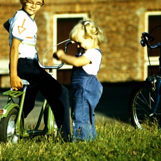 Three children playing with bicycles outdoors.
