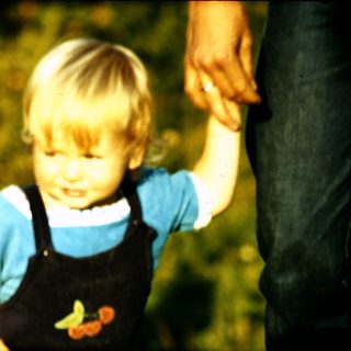 Young child holding adult's hand outdoors.