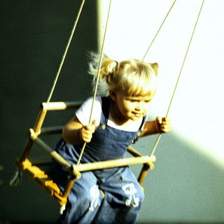 Young girl swinging happily on a rope swing.