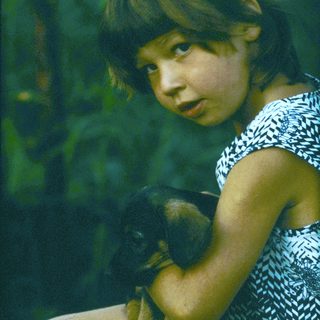 Young girl holding a small black kitten outdoors.