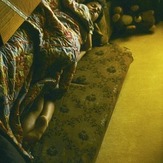 Person resting on patterned bed with warm lighting.