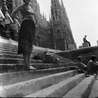 Woman posing on cathedral steps with suitcase.